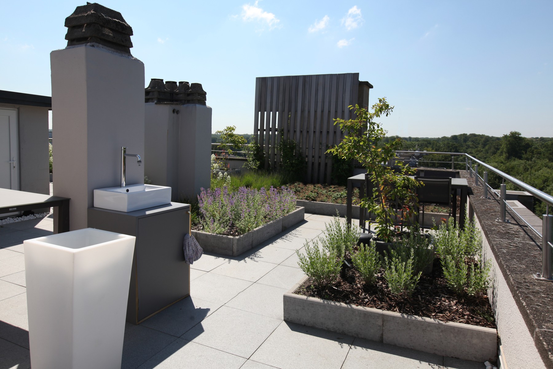 Dachterrasse mit einem Außenwasserhahn auf einem Sockel, einem beleuchteten Pflanzkübel und Pflanzbeeten mit Lavendel
