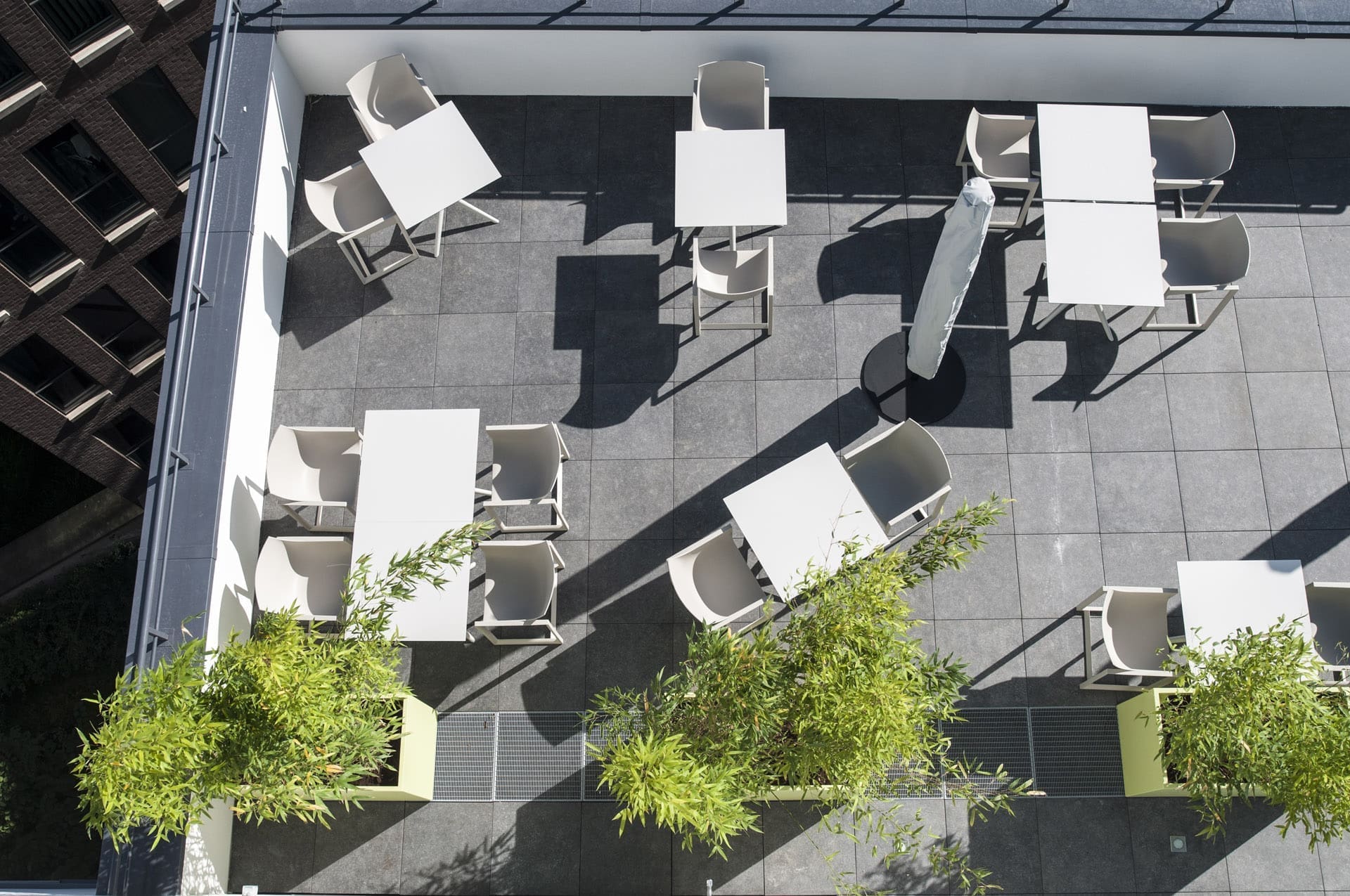 Luftaufnahme einer Dachterrasse mit weißen Tischen und Stühlen zwischen Pflanzkübeln mit Bambus
