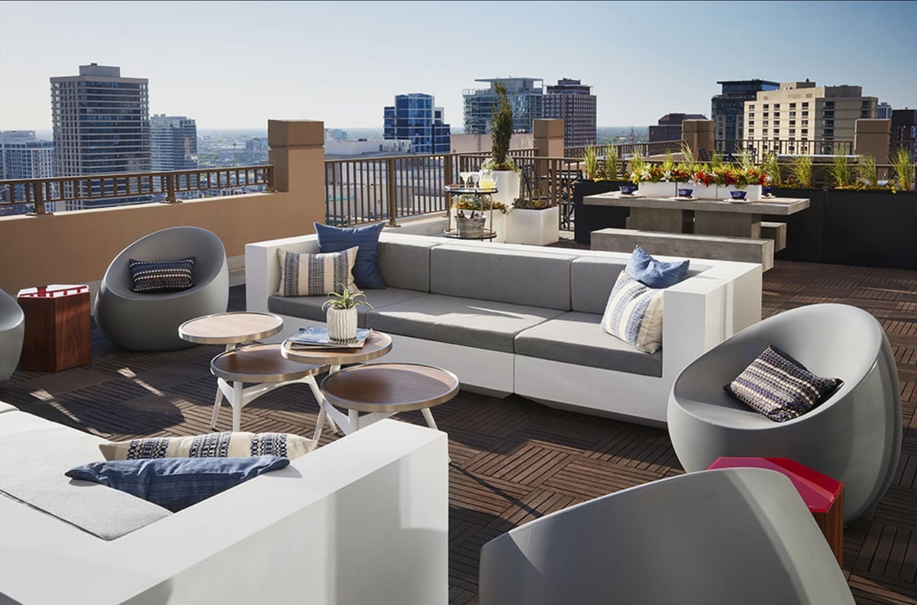 Loungeecke auf einer Dachterrasse mit weißen Bänken, runden grauen Schalensesseln und blauen Kissen auf einem Holzdeck