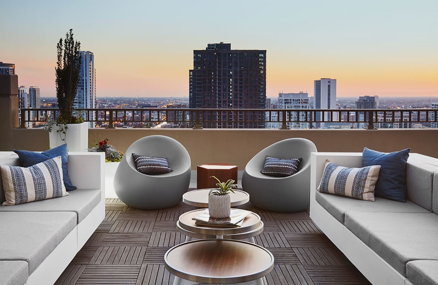Dachterrasse bei Sonnenuntergang mit weißen Loungebänken, runden Schalensesseln und niedrigen runden Beistelltischen