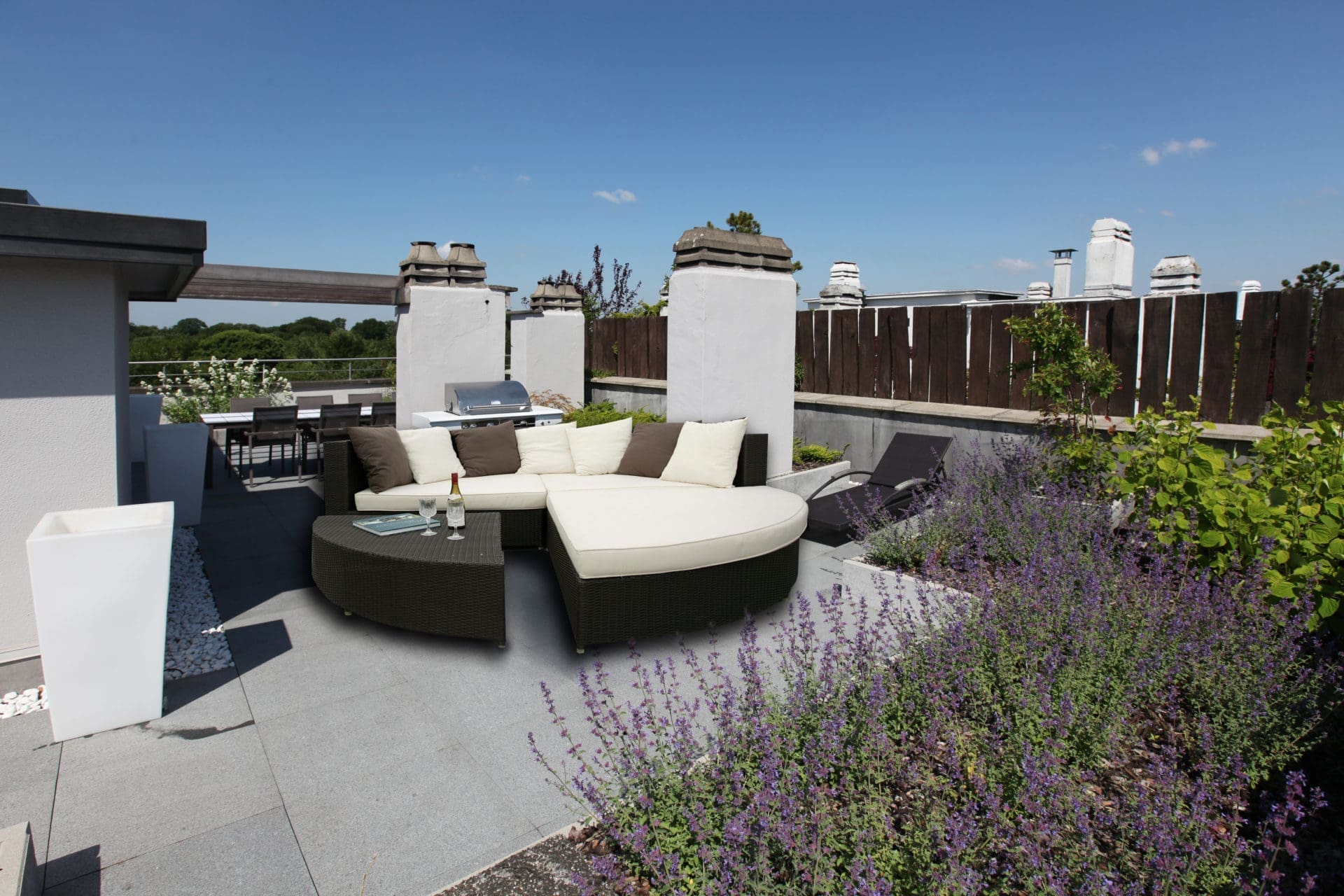 Rundes Daybed aus Rattan mit weißen Kissen auf einer Dachterrasse neben einem Pflanzbeet mit violetter Katzenminze