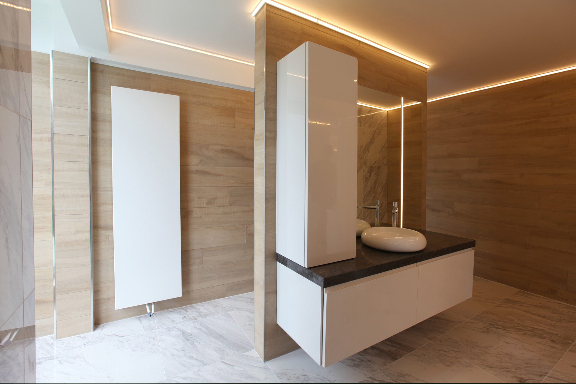 Badkamer met wandtegels in houtlook, een wit hooglans meubel met donker natuurstenen blad en een vloer in marmerlook