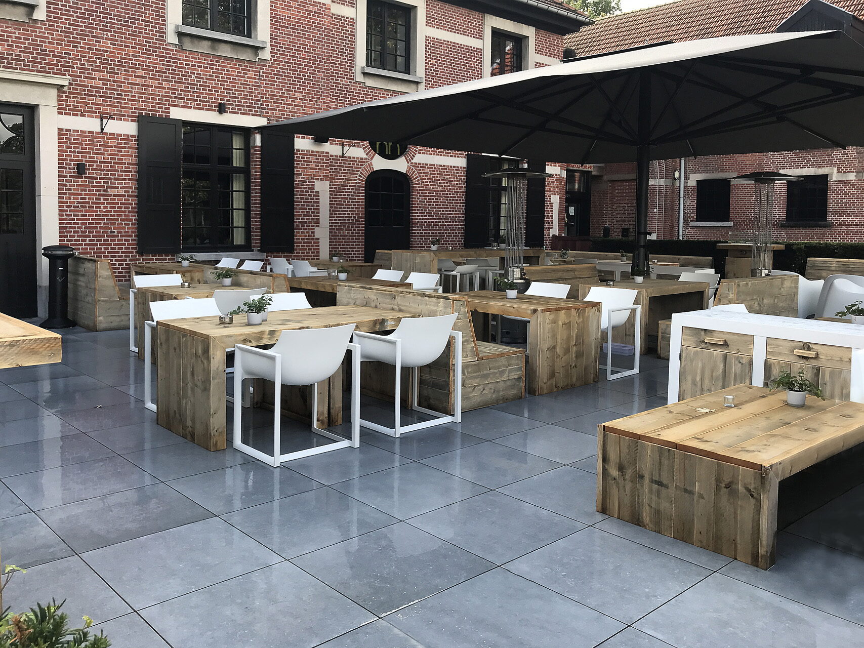 Terrasse mit hölzernen Tischen, weißen Schalensesseln und schwarzen Sonnenschirmen