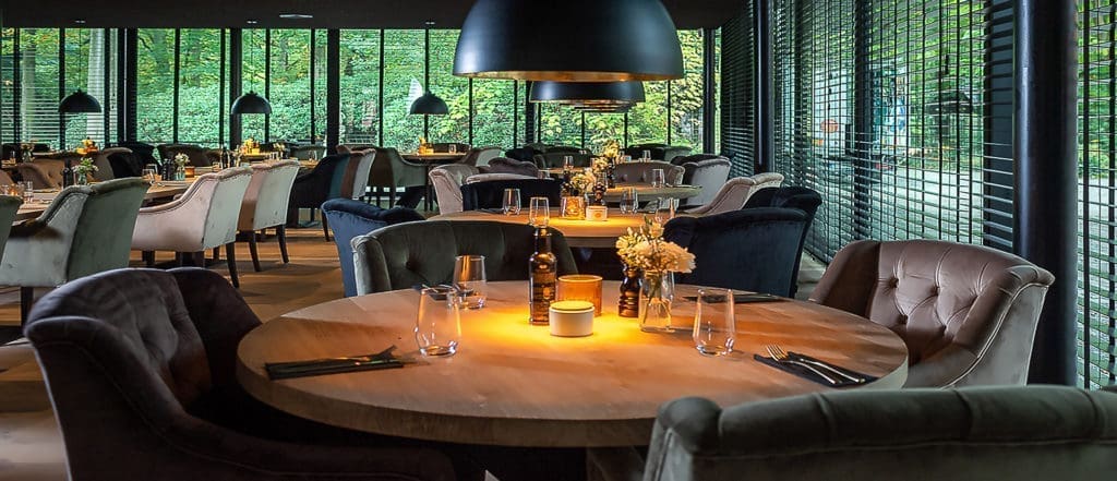 Restaurantzaal met ronde tafels, fauteuils in velours en zwarte hanglampen