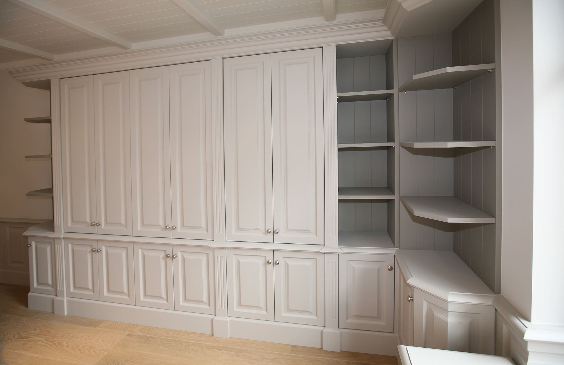 A white cabinet wall with panelled doors and open corner shelves.