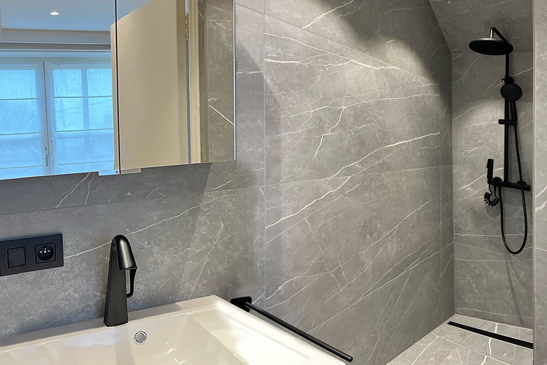 Badkamer met wanden in grijze marmerlook, een ligbad met zwarte kraan en een inloopdouche met zwarte regendouche