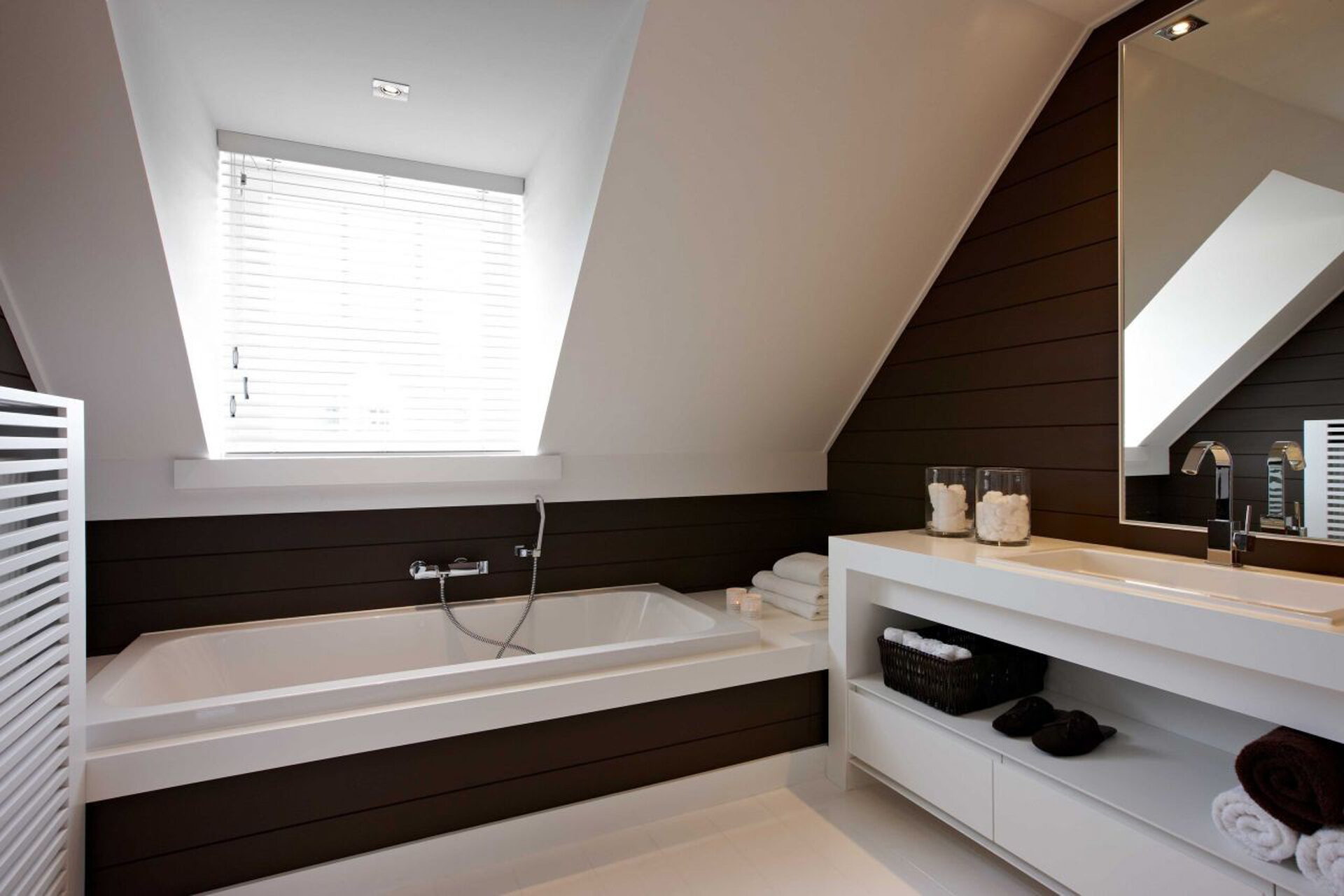 Badkamer onder een schuin dak met een ligbad en een lange wastafelkast