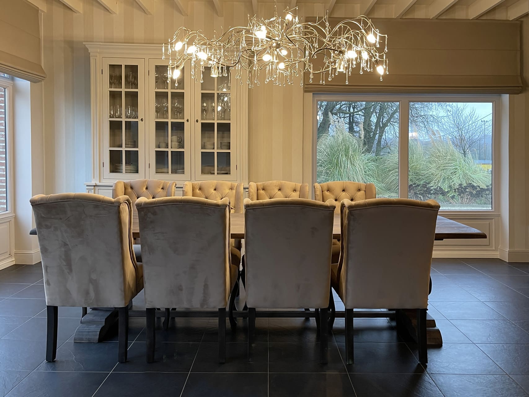 Salle à manger avec un lustre en forme de branches et pampilles en cristal au-dessus d'une table avec des chaises en velours gris et ocre