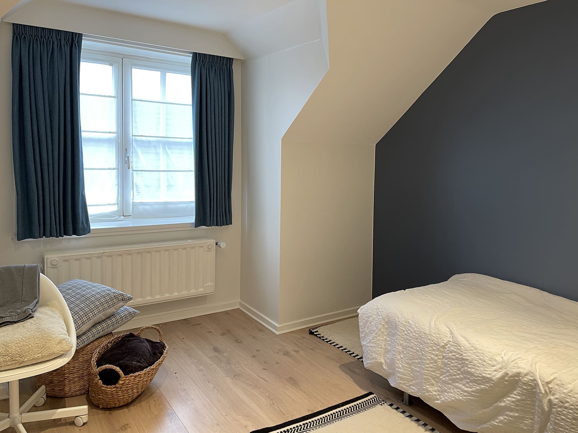 Kleine slaapkamer met een donkerblauwe dakschuinte en gordijnen in dezelfde kleur, woning bij Brussel