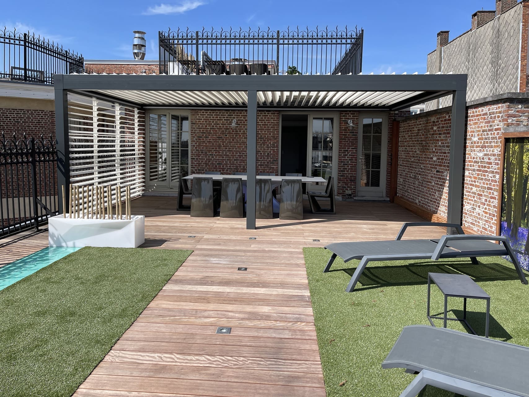 Dachterrasse mit einer Aluminium-Pergola, einem Außentisch, Liegen auf Kunstrasen und einem Holzdeck