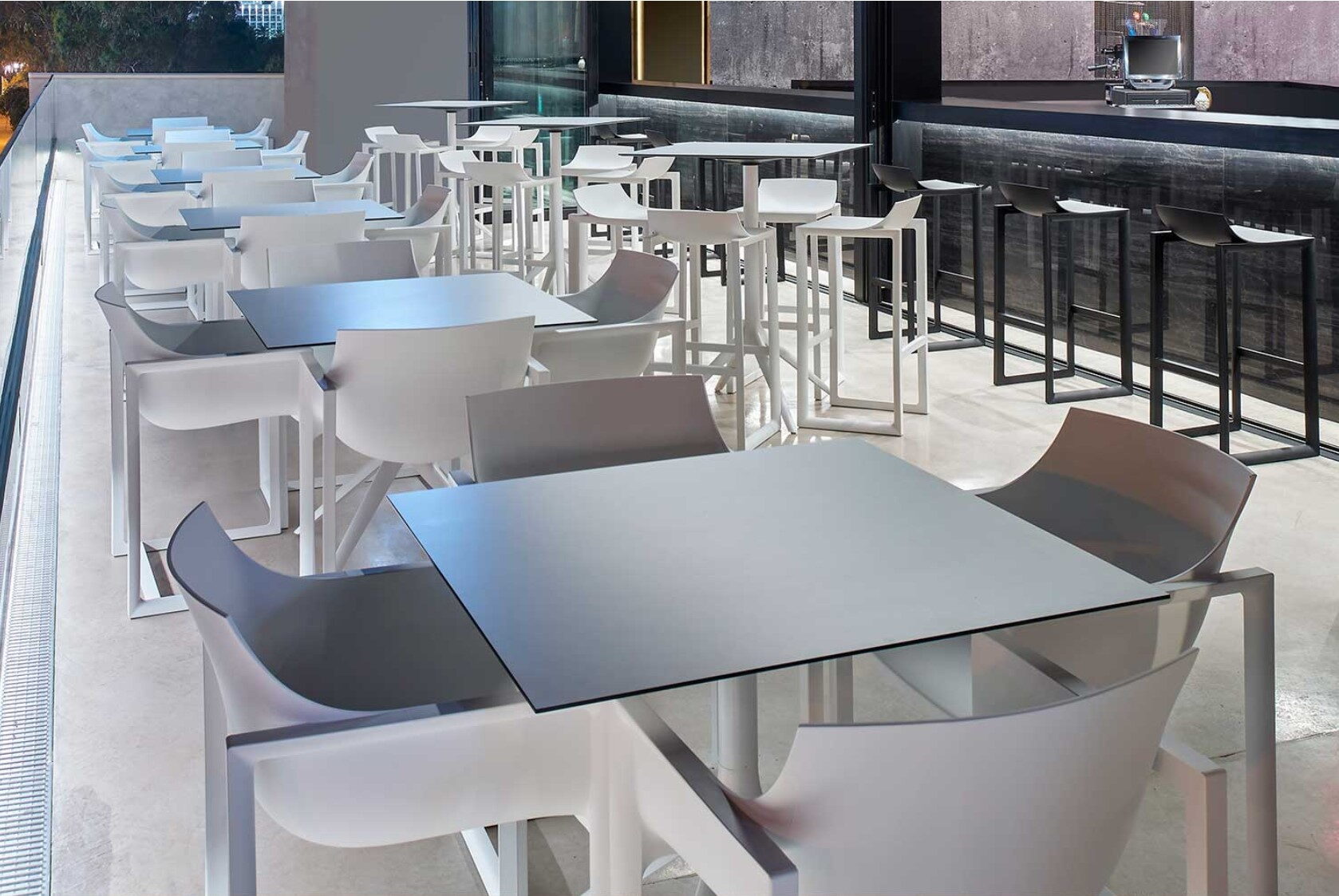 Dachterrasse mit weißen Tischen, Schalensesseln und einer Betonbar