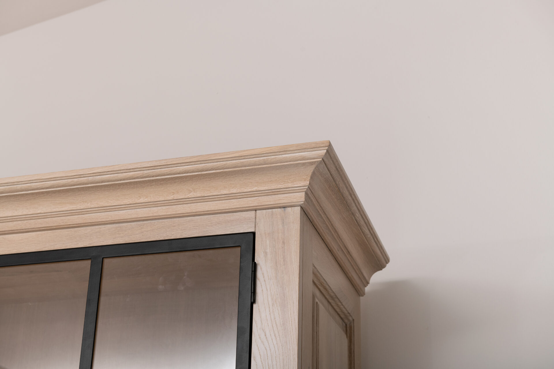 Detail van een lichte eiken kroonlijst boven een kastdeur met een zwart stalen glaskader