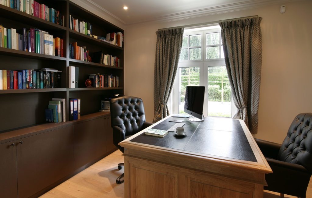 Donkere boekenwand vol boeken en mappen rond een raam, met een houten bureau ervoor