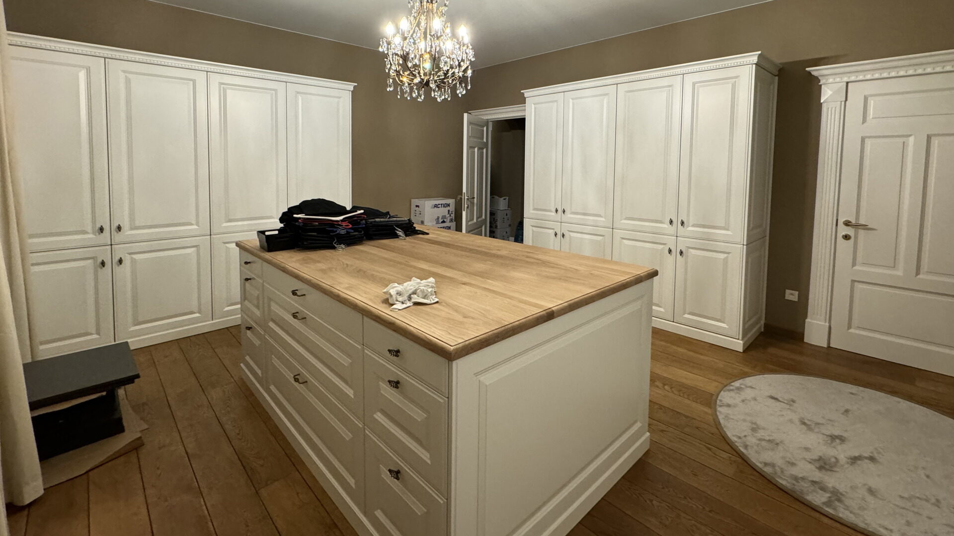 Dressing met witte kastenwanden met panelen deuren rond een eiland met een eiken blad, onder een kroonluchter
