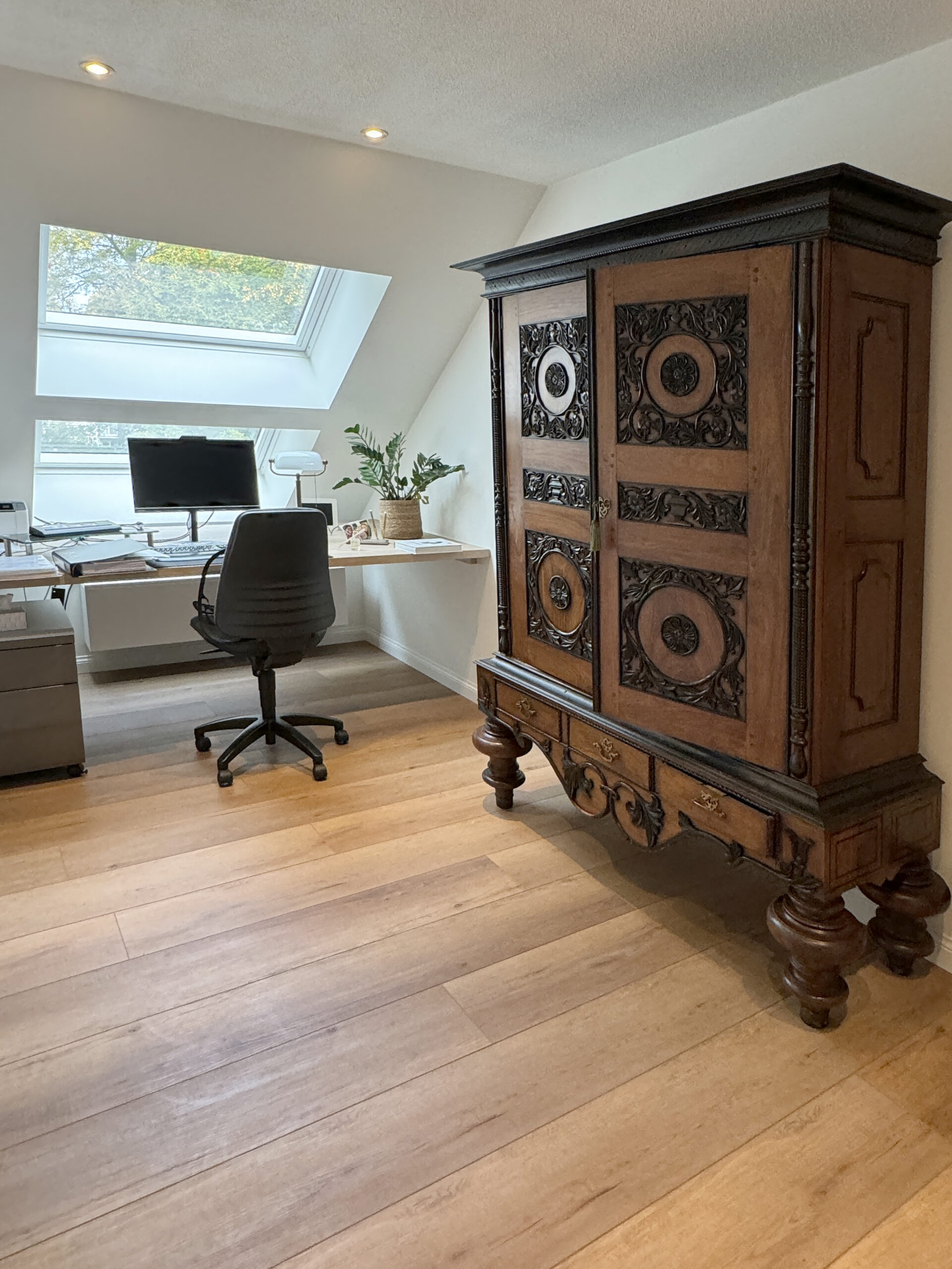 Antieke gesculpteerde eiken kast naast een modern ingebouwd bureau op de zolder