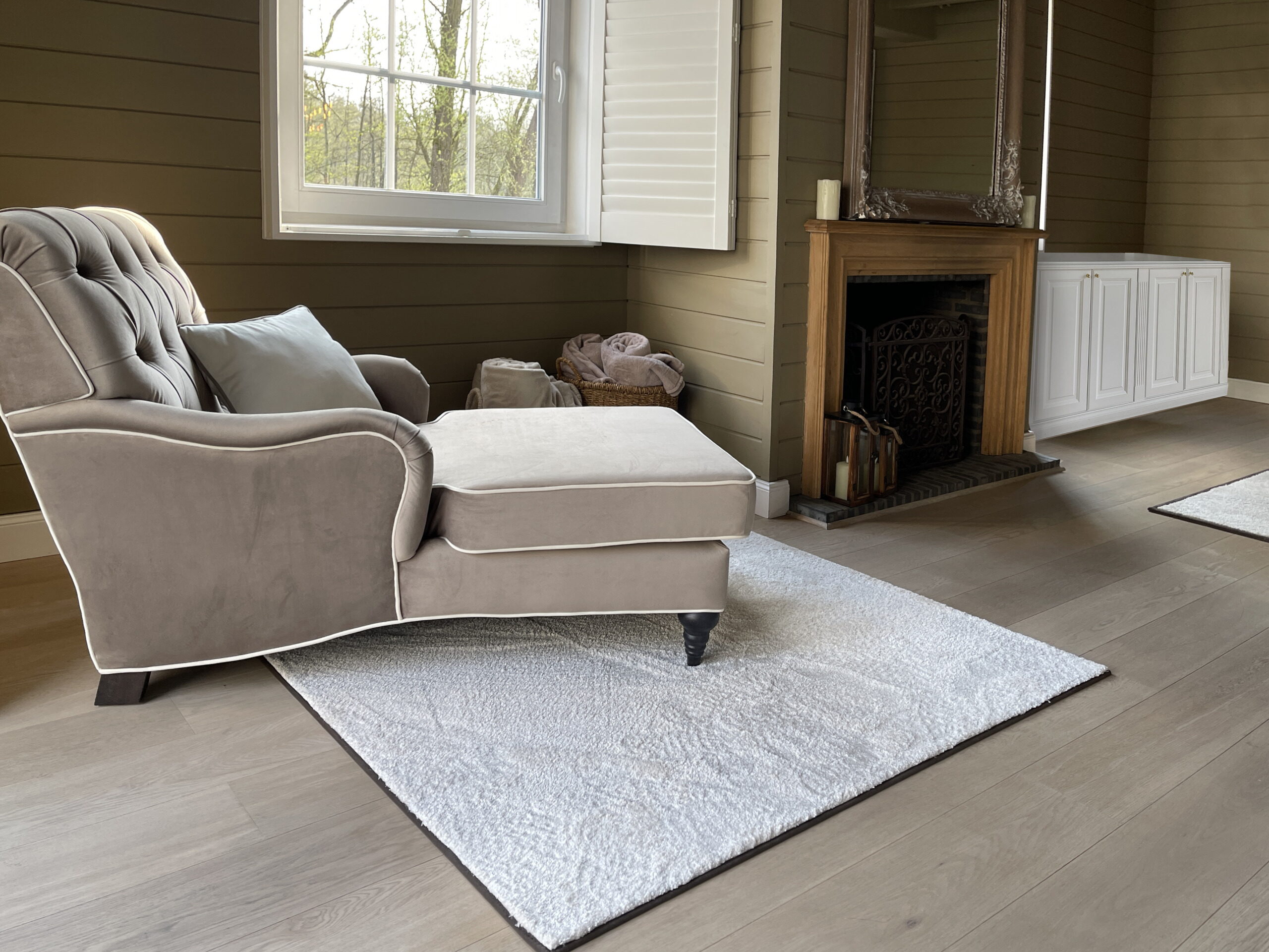 Fauteuil met voetbank in taupe velours naast de open haard