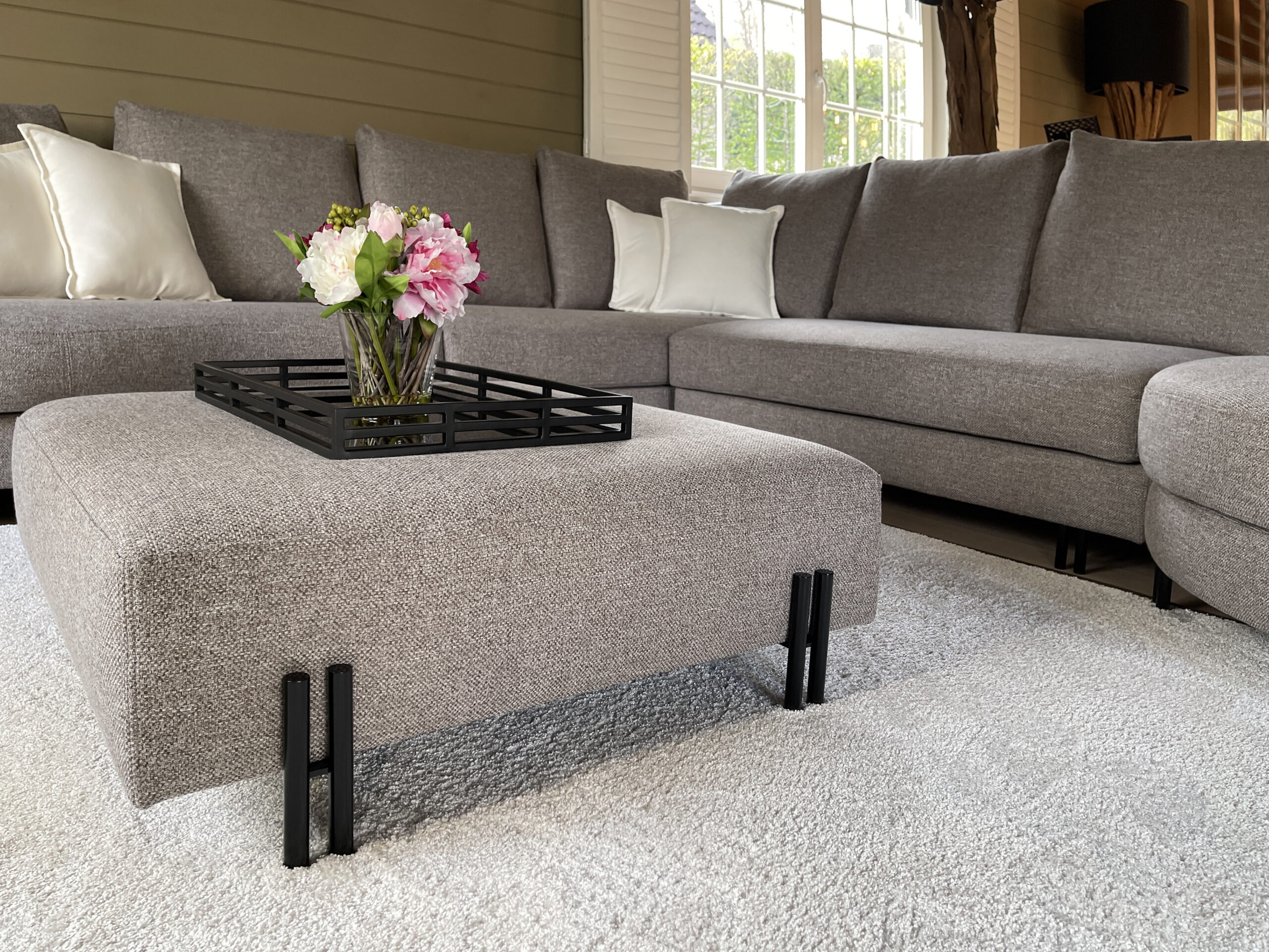 Gestoffeerde poef met zwart dienblad en bloemen voor de hoeksofa