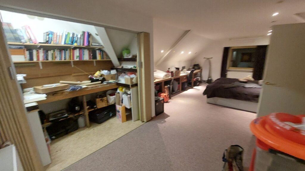 De zolder voor de verbouwing, met een oude werkbank, boekenplanken en tapijt