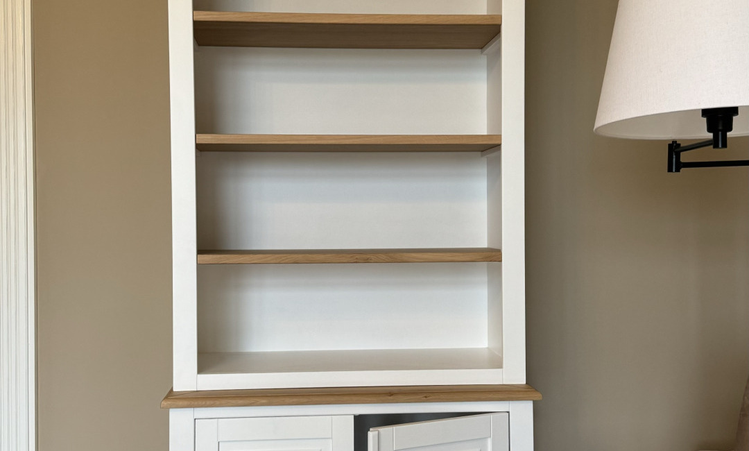 Witte boekenkastnis met eiken legplanken en een zwarte wandlamp ernaast