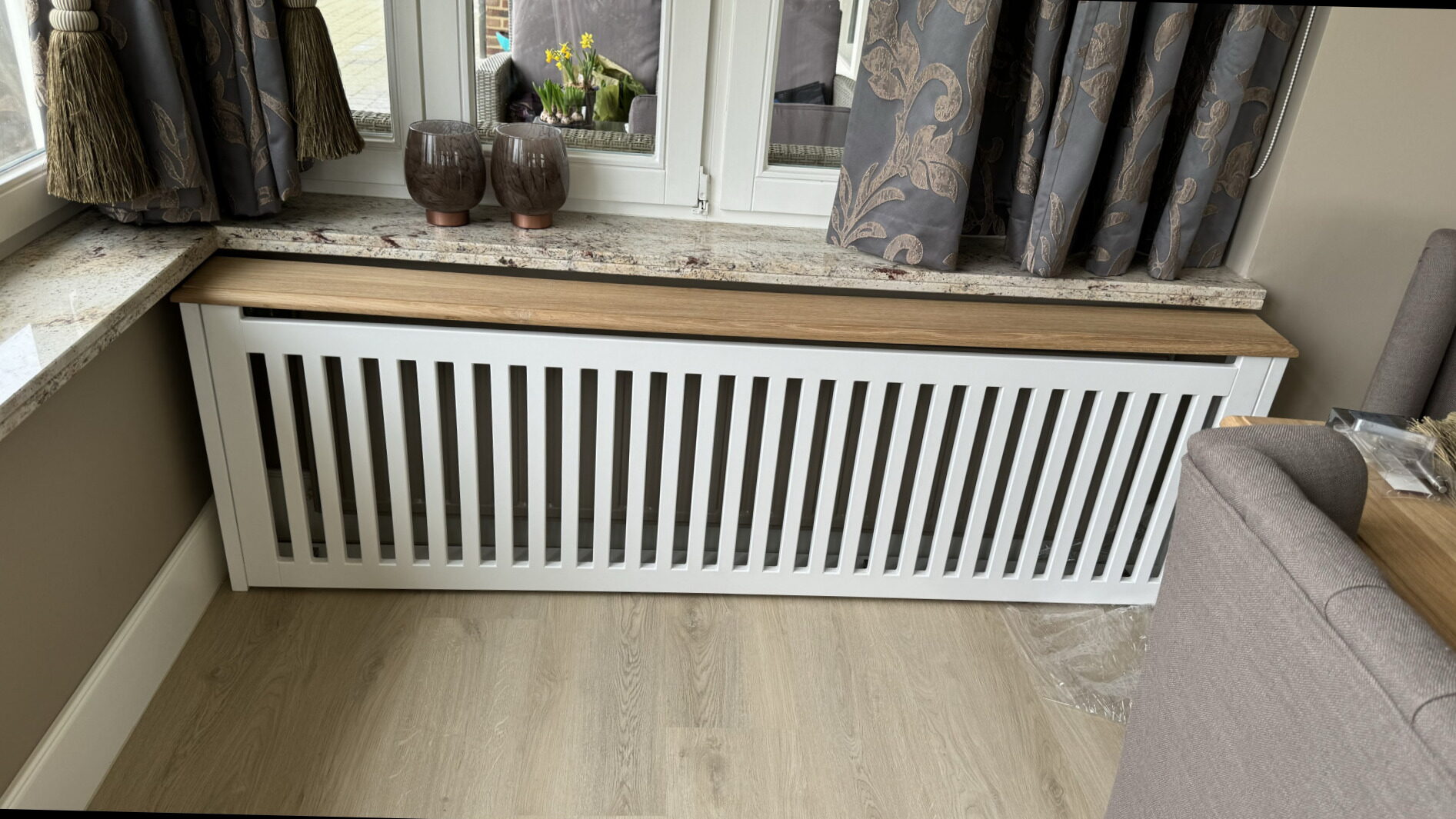 Witte radiatorombouw met verticale latten en een eiken tablet onder een raam met een natuurstenen dorpel