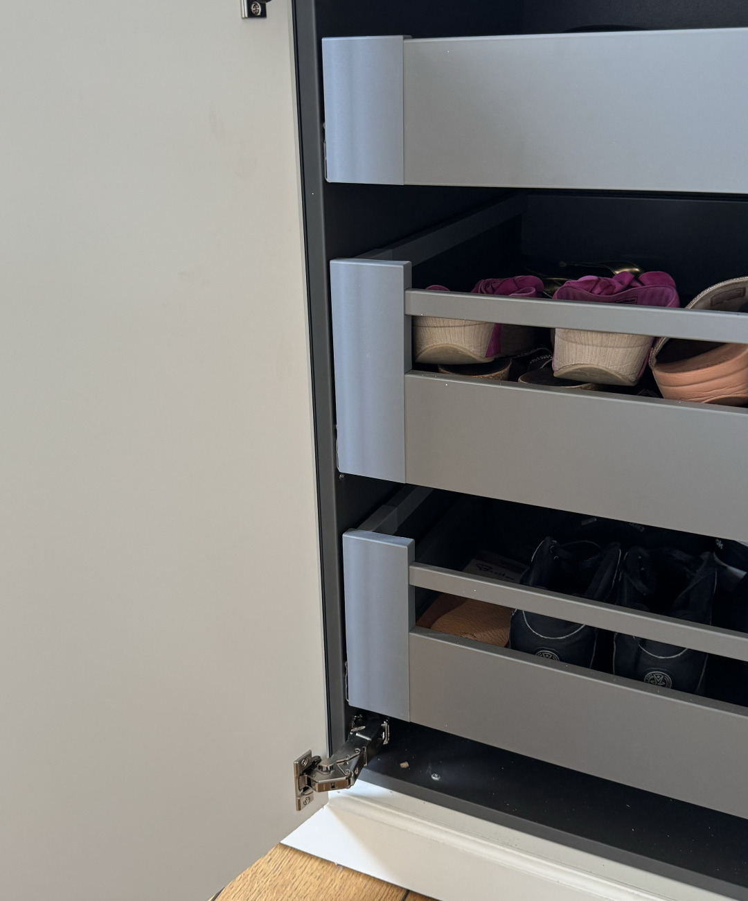 Uitschuifbare lades achter een kastdeur, gevuld met schoenen