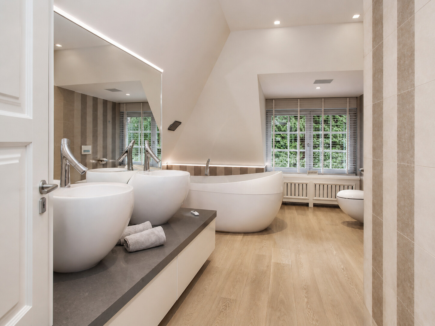 Badkamer met dubbele wastafel, vrijstaand bad bij het raam en hangtoilet