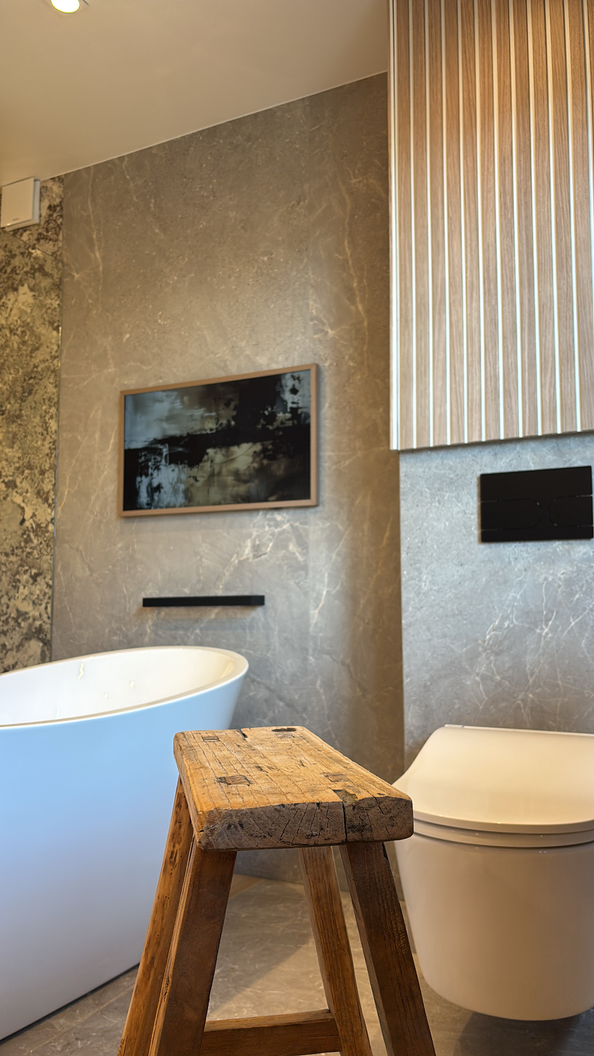 Zwevend toilet naast het vrijstaande bad, met een houten krukje en een televisie die een kunstwerk toont