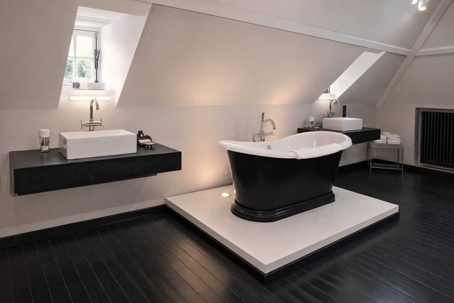 Badkamer onder het dak met een zwart vrijstaand bad op een verhoog in lichte steen