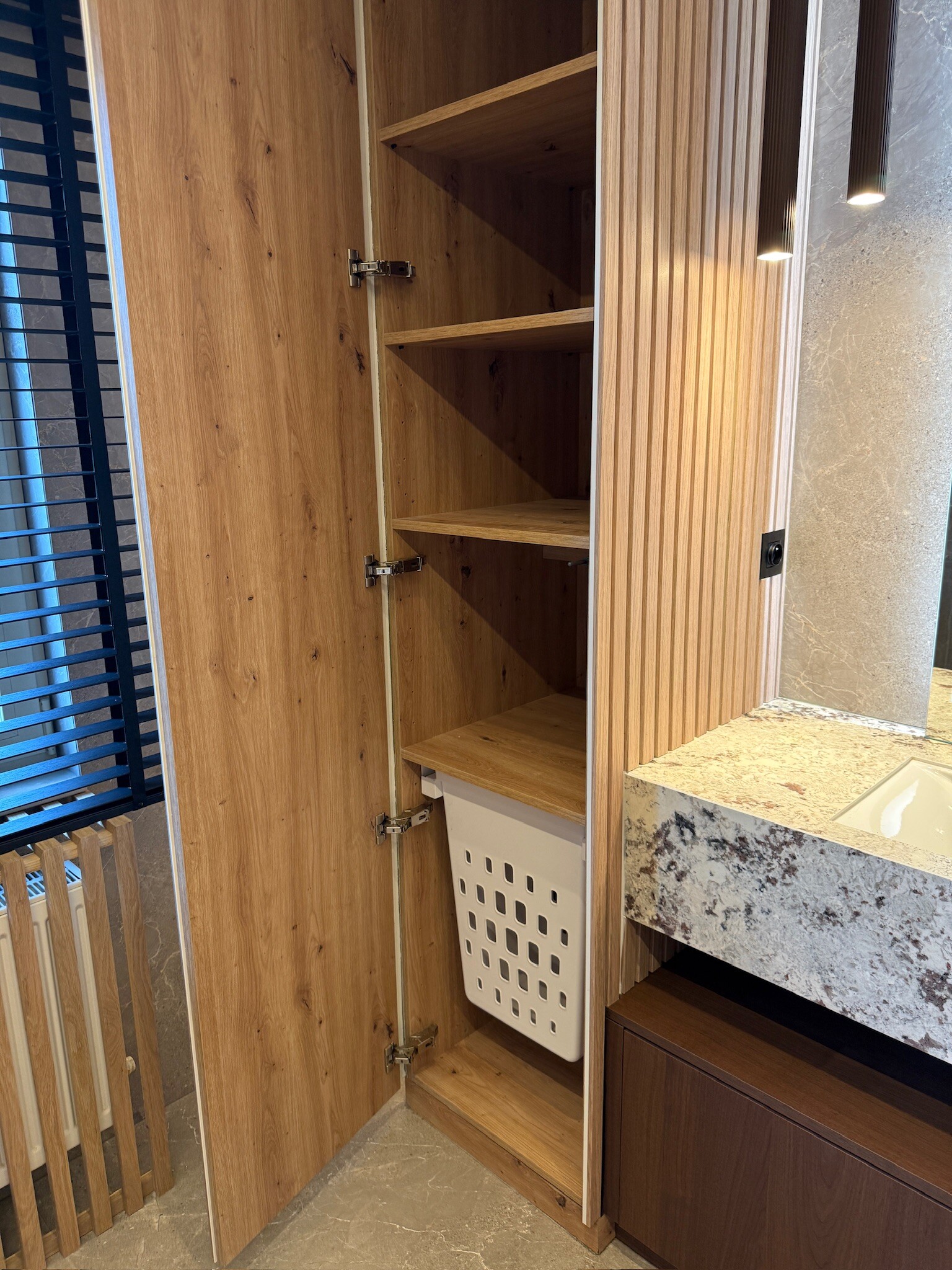Hoge badkamerkast op maat in eik met open legplanken en een uitneembare wasmand