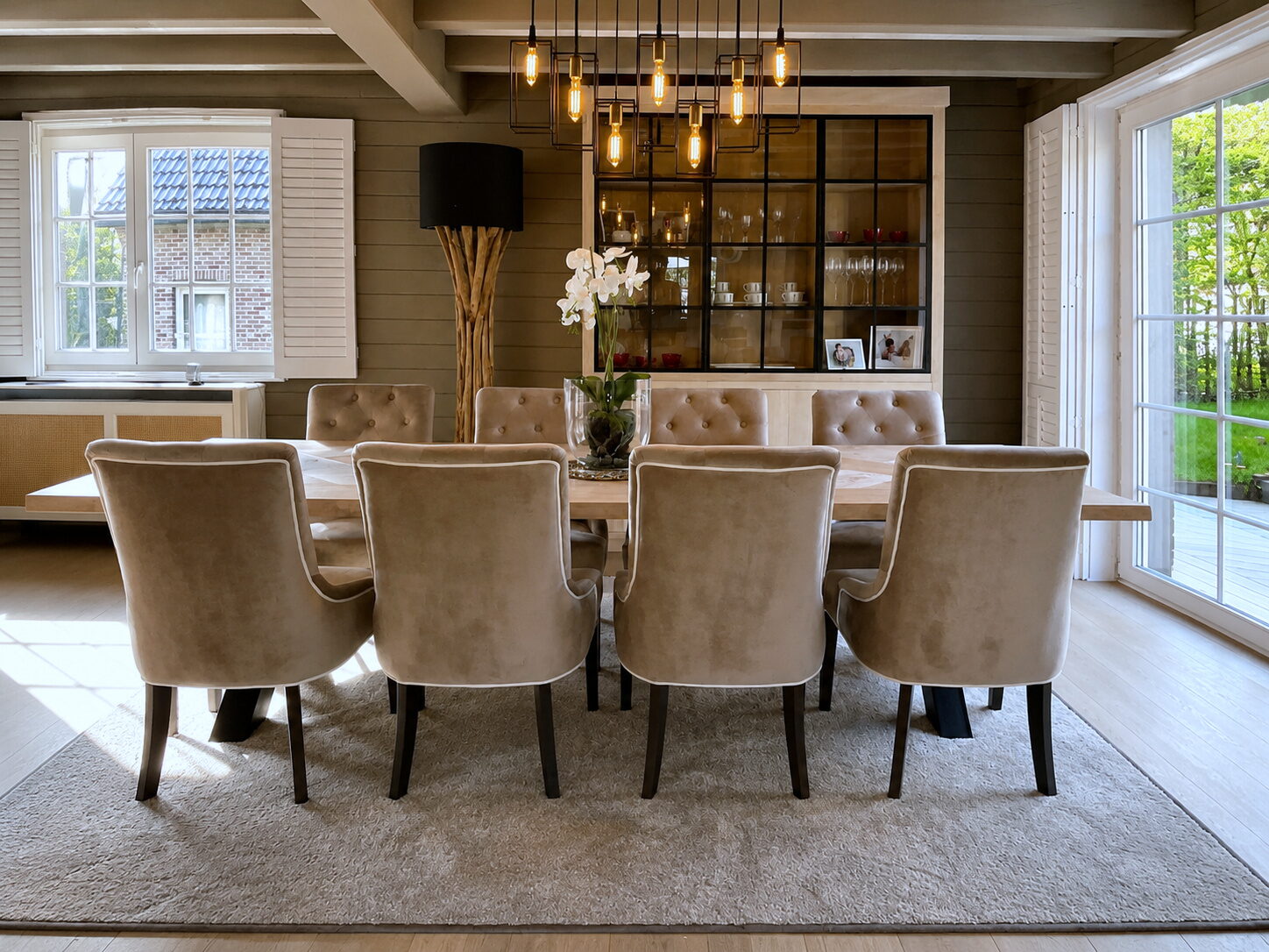 Eetkamer met een zwart omkaderde vitrinekast met glasdeuren achter een tafel met hanglampen