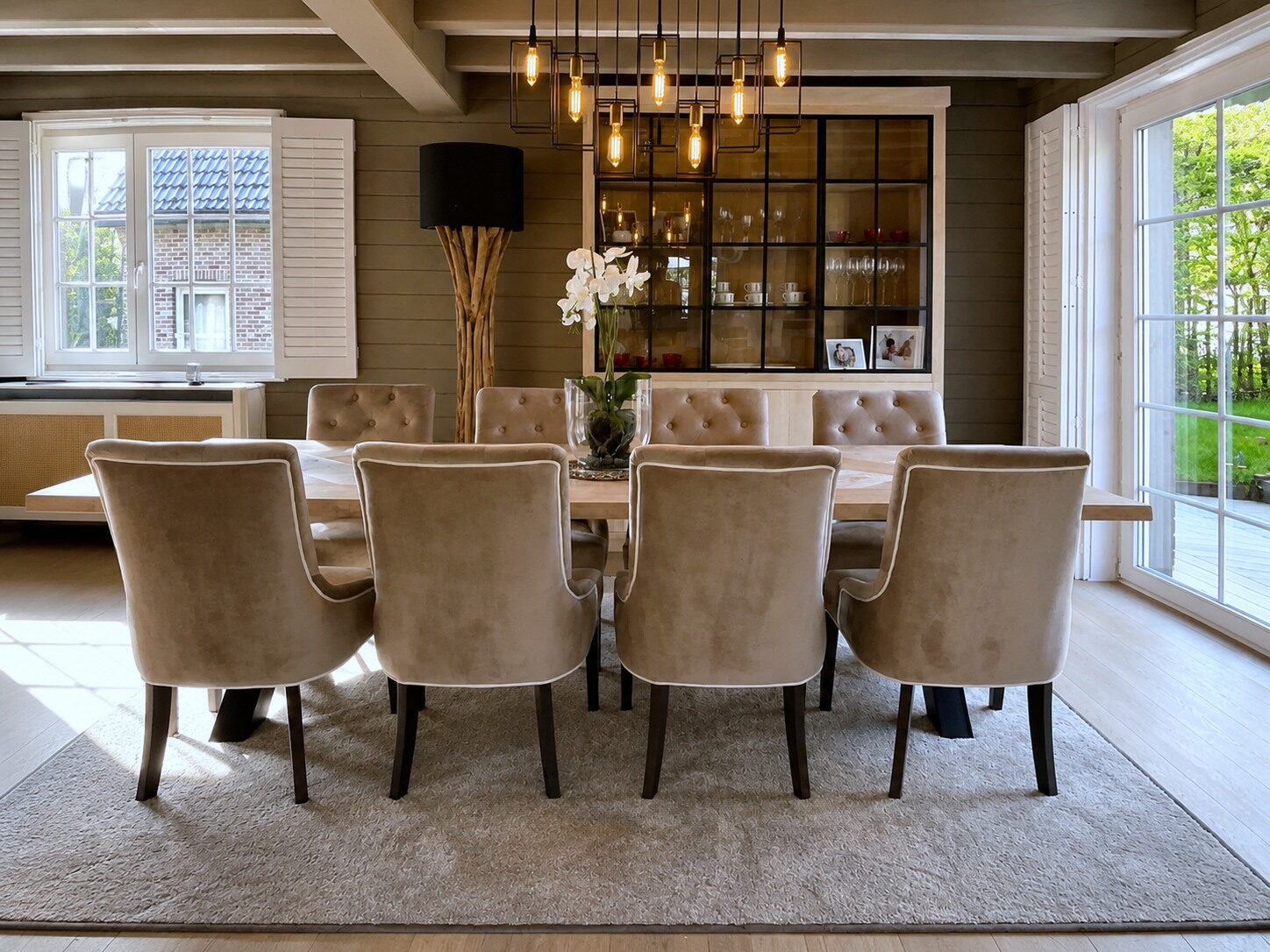 Eetkamer met een lange eiken tafel, gecapitonneerde stoelen en een vitrinekast met zwarte roeden