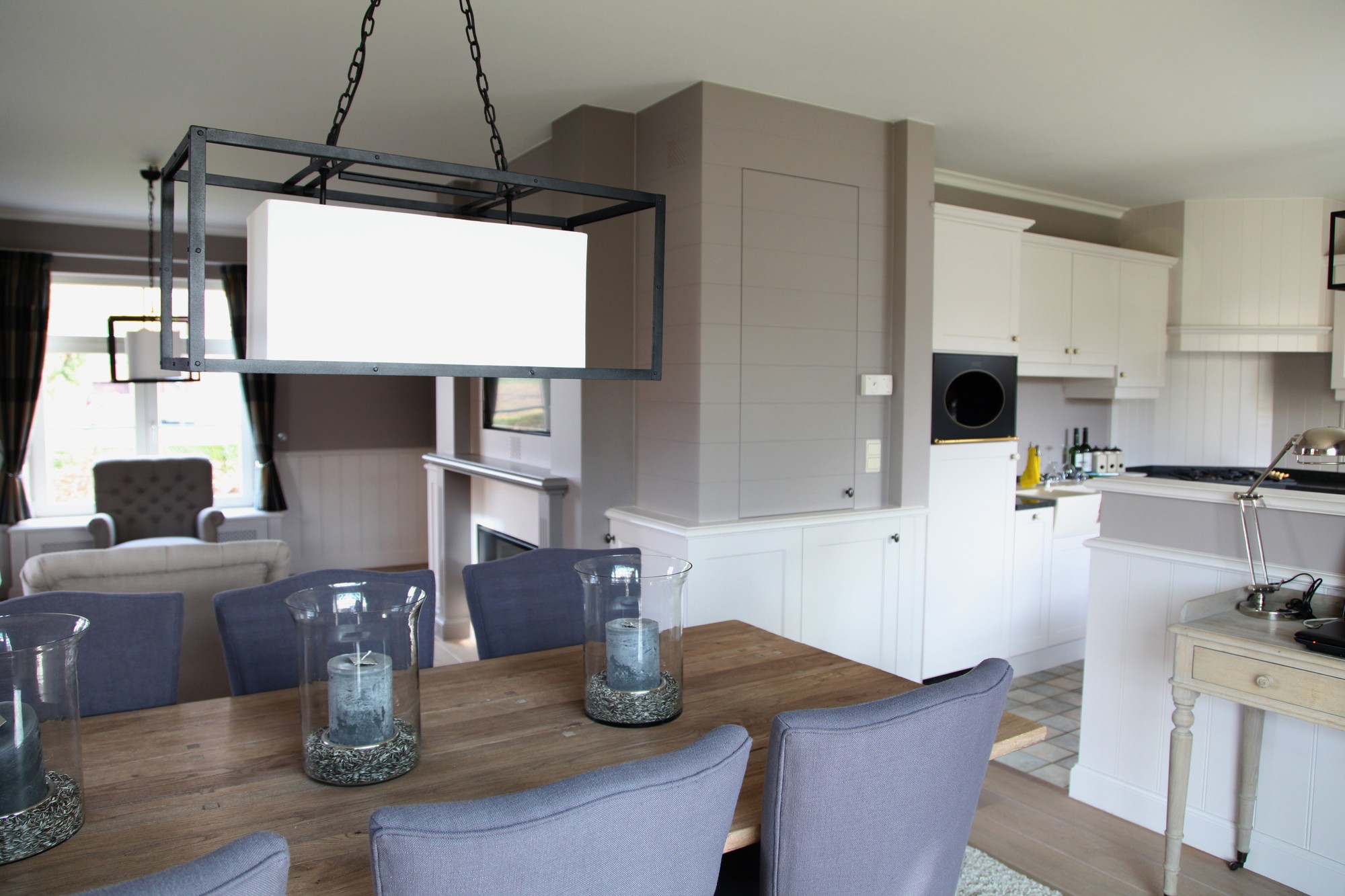 Eettafel met glazen windlichten onder een hanglamp met zwart frame