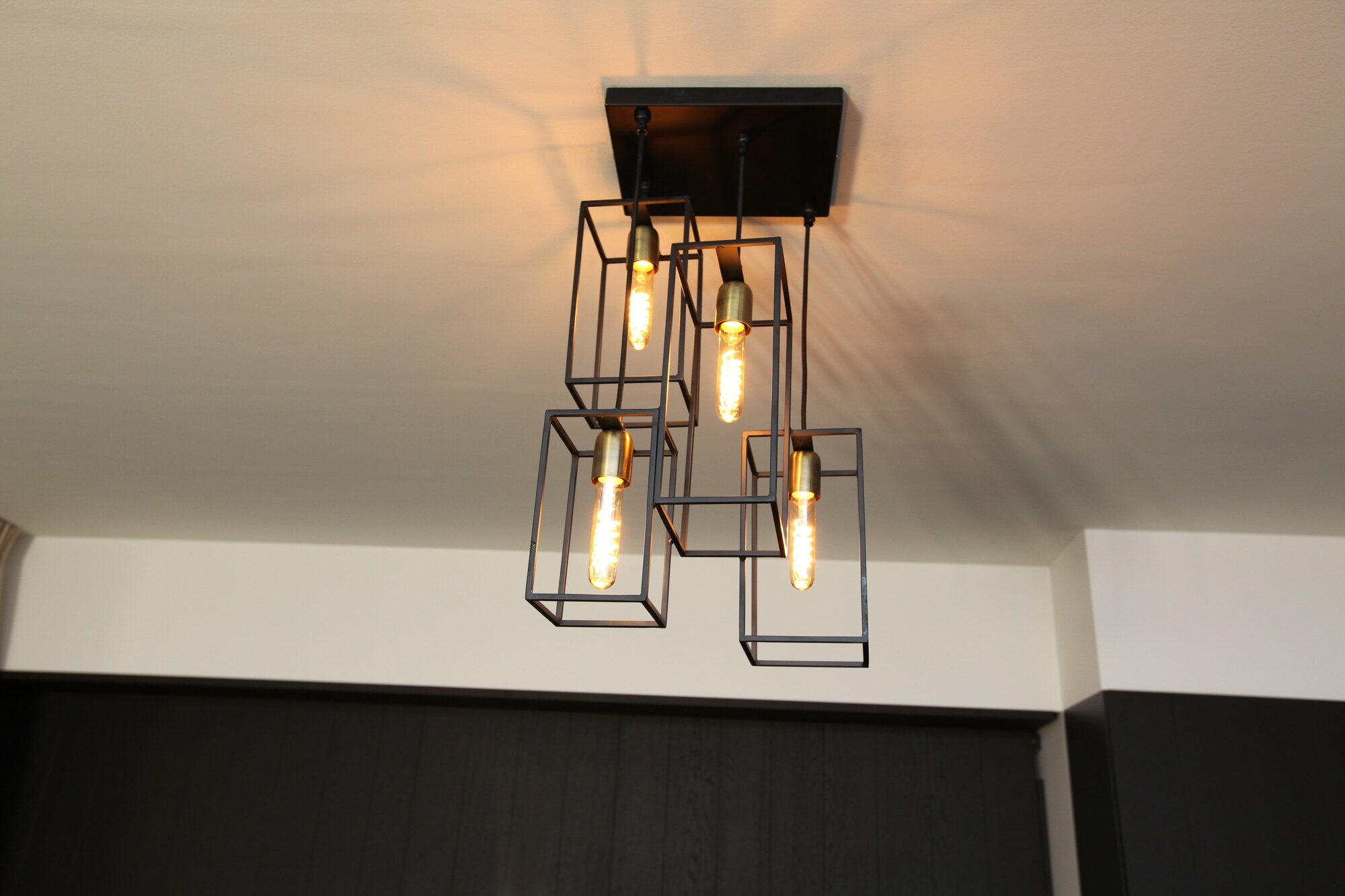 Hanglamp opgebouwd uit open zwarte kubussen met zichtbare gloeilampen