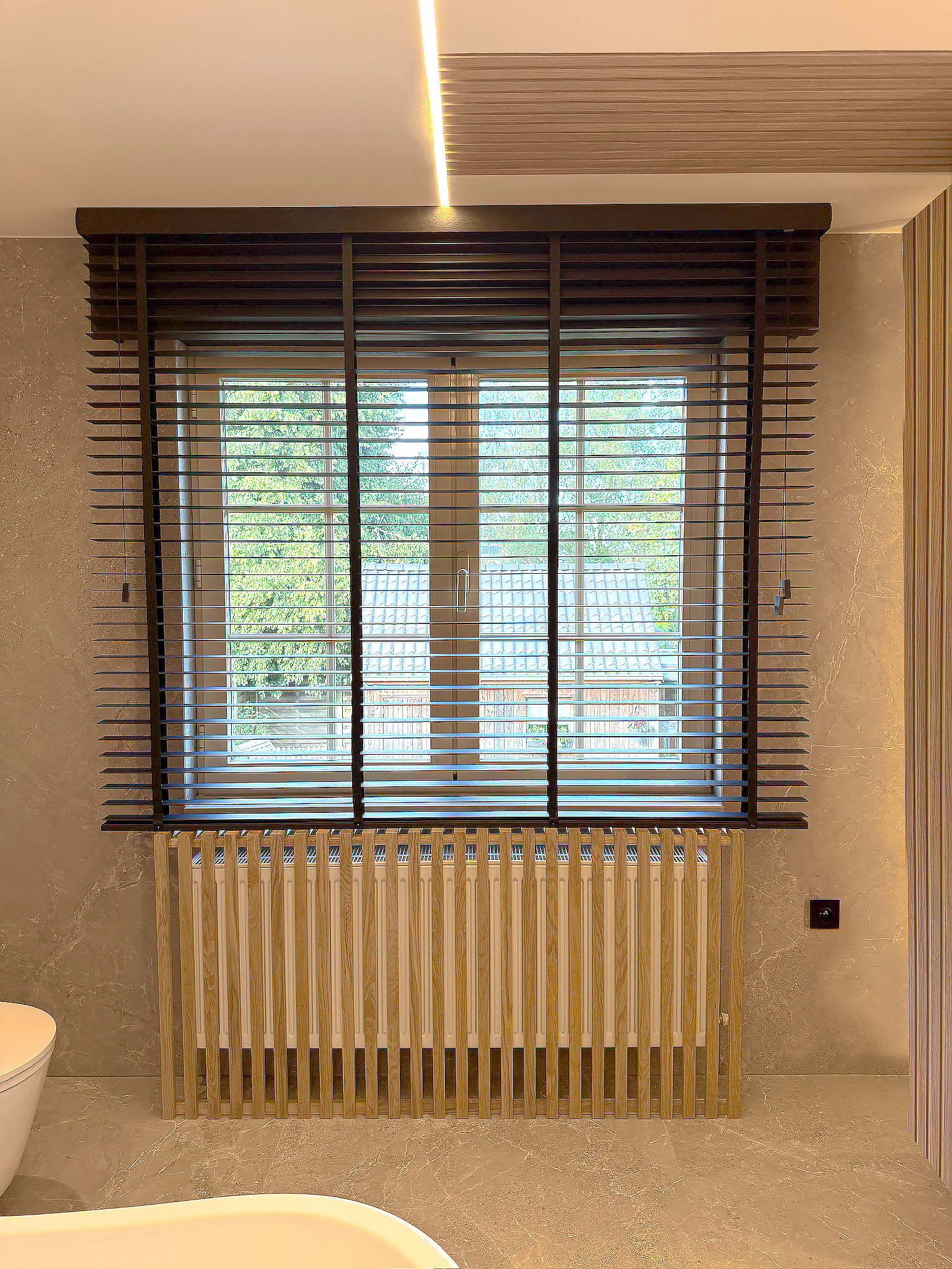 Radiatorombouw in eiken latten onder het raam met zwarte jaloezie, badkamer in Westerlo