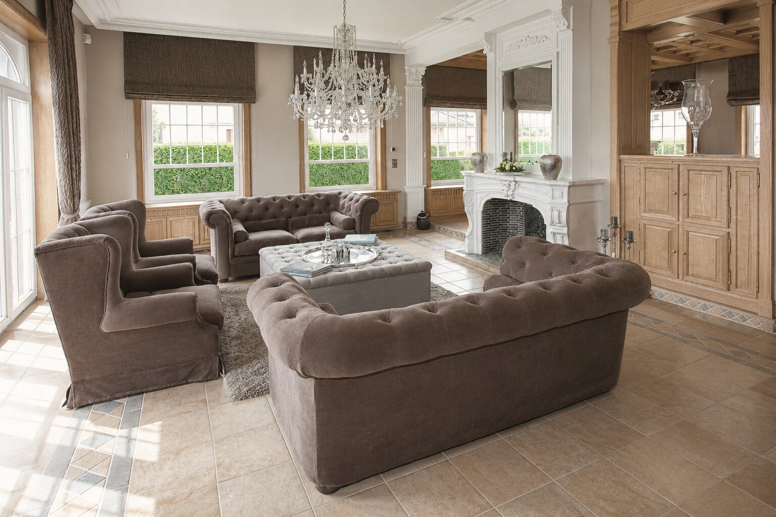 Salon met chesterfields tegenover een open haard in lichte steen