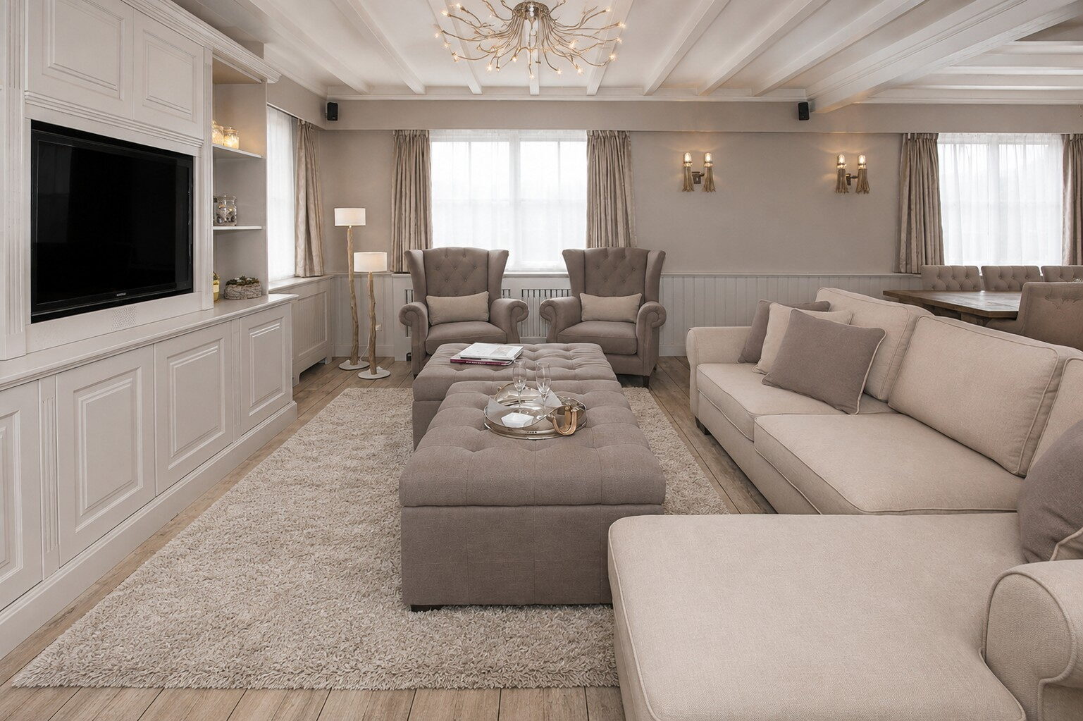Salon met tv-wand, oorfauteuils, poef en luchter onder de balken