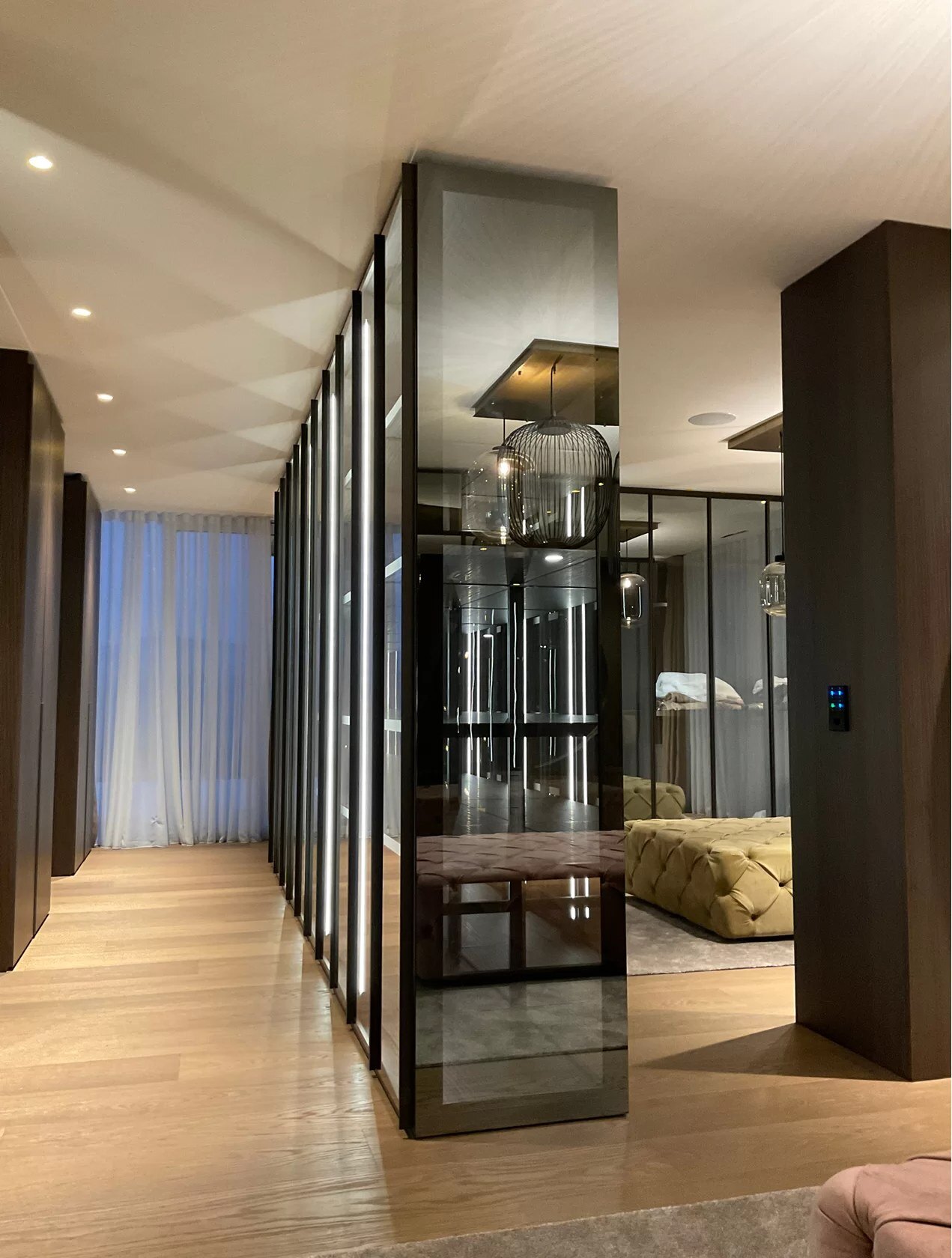 Vrijstaande kast in glas met een donker kader die de gang van de slaapkamer scheidt, op een houten vloer