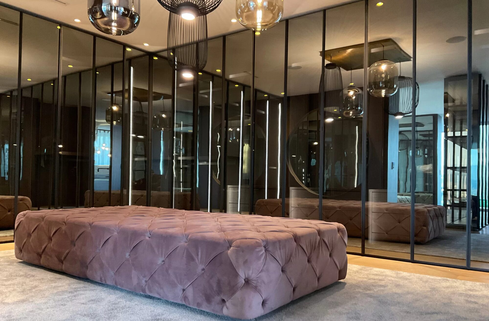 Schlafzimmer mit einer Ankleide hinter getöntem Spiegelglas und einer kapitonierten Bettbank