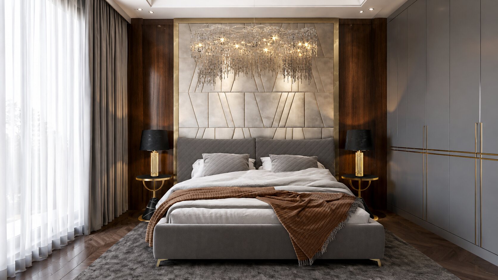 Slaapkamer met een grijs gecapitonneerd bed voor een messingkleurig wandpaneel, een kroonluchter en notenhouten zijpanelen