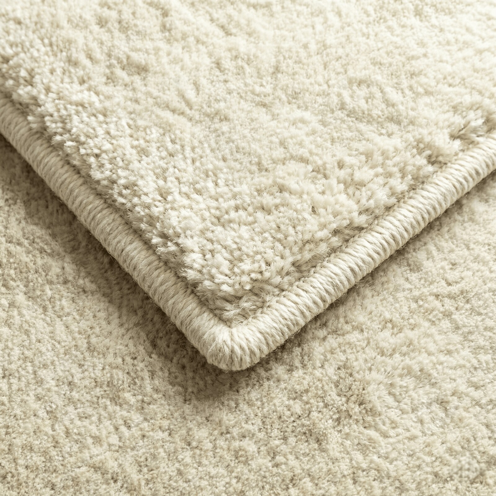 Angle d'un tapis crème à poils longs, replié pour laisser voir la rive bordée