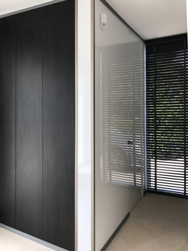 Een houten jaloezie voor een raam in een gang, met de lamellen half gekanteld.