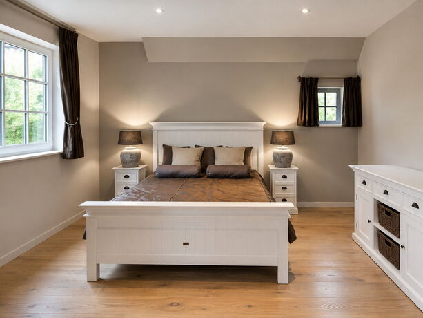 Een logeerkamer met een wit houten bed en nachttafels in dezelfde witte uitvoering.