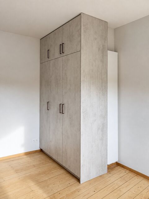 Een inbouwkast met fronten in betonlook die met een blinde zijwand de hoek van de kamer afwerkt.