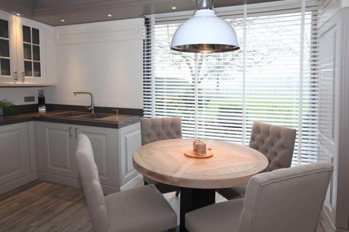 Een hanglamp in wit emaille die recht boven een ronde eettafel hangt.