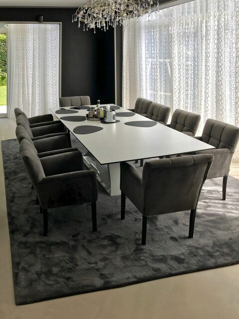 Een eettafel op een hoogpolig tapijt, met een kroonluchter recht boven het blad.