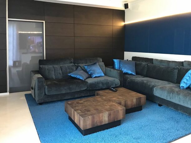 Een hoekzetel in donker velours met helderblauwe kussens, op een blauw tapijt.