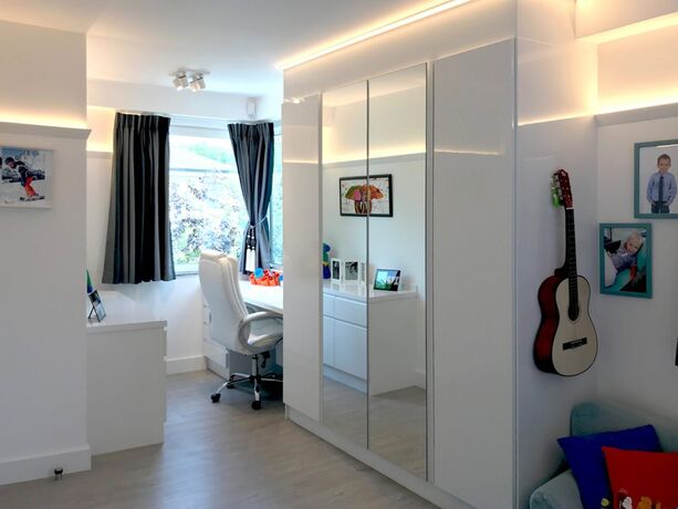 Een kinderkamer waarin het bureaublad is ingebouwd in de kastenwand naast het bed.