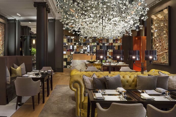 Een restaurantzaal met een tapijt over de volle vloer, gestoffeerde stoelen en een grote luchter.
