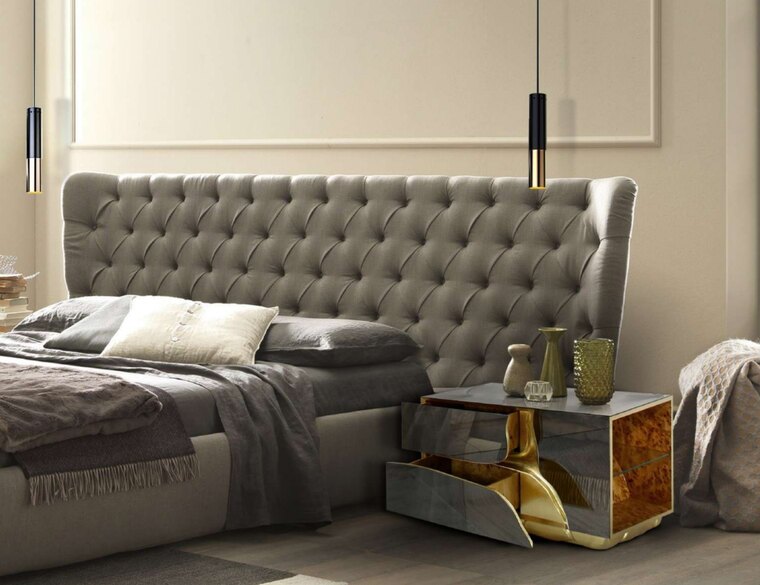 Détail d'une haute tête de lit capitonnée en tissu gris clair, avec des joues relevées de part et d'autre du lit.
