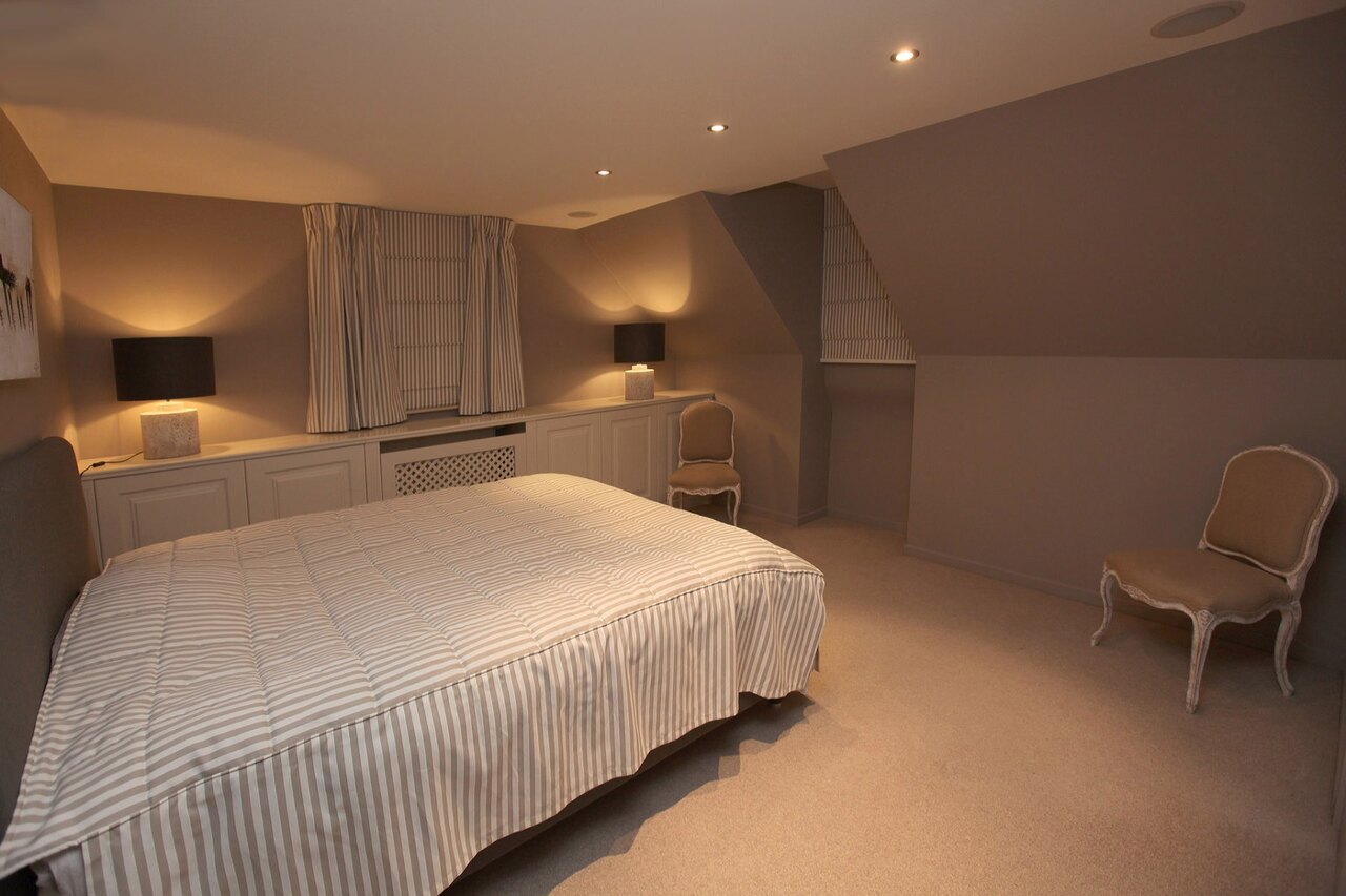 Une chambre sous pente avec un lit contre le mur bas, des armoires encastrées dans la pente et un cache-radiateur sous la fenêtre.